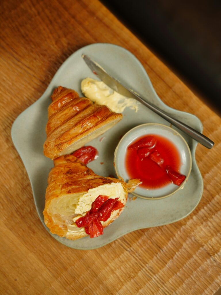 Top view of a croissant with butter and red jam on an artistic plate.