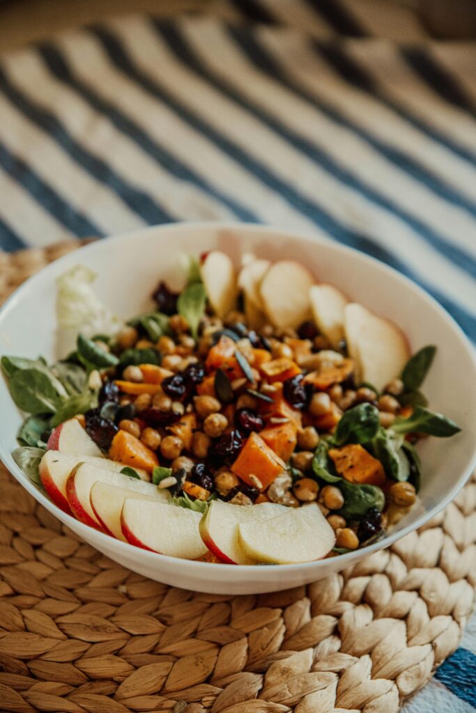 Delicious chickpea salad with apples, raisins, and greens served in a stylish white bowl.