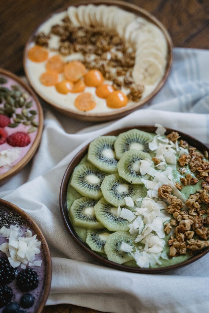 Three vibrant breakfast bowls with fresh fruits and granola on a wooden table.